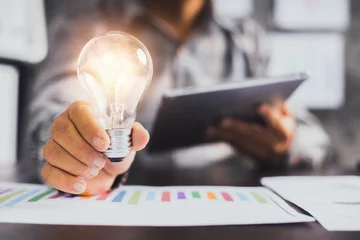 Foto auf Acrylglas Büro Erfolgreiche Geschäftsidee und kreatives Innovationskonzept, Nahaufnahme Geschäftsmann, der Glühbirne und Tablet mit Finanzdiagramm auf dem Tisch hält