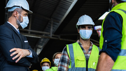 Industrial worker and engineer stand in line to check flu with infrared thermometer before enter to work and protect Coronavirus or Covid-19, safety and protection as working in manufacturing