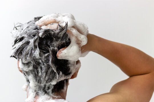 A man washes his head with shampoo on white background, rear view