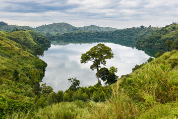 A small lake with reflected clouds on its still surface surrounded with rich vegetation and farm...