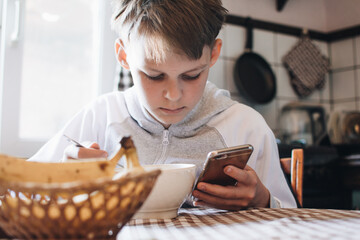 The boy plays on the phone during breakfast. Addiction to gadgets and smartphones. Breakfast before school in the kitchen.