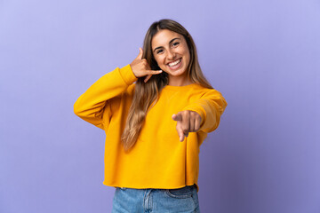 Young hispanic woman over isolated purple background making phone gesture and pointing front