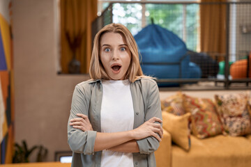 Portrait of a young surprised woman, female office worker keeping mouth opened and looking at camera while standing in the modern office