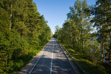 Asphalt freeway through summer forest near lake