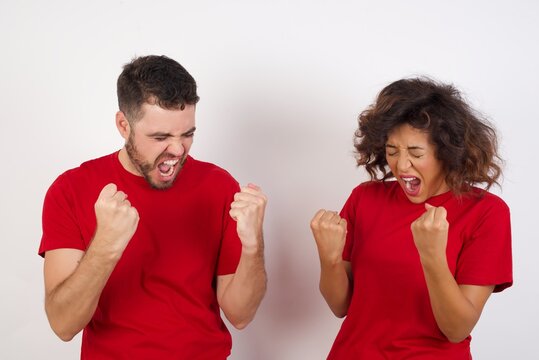 Young Beautiful Couple Wearing Red T-shirt On White Background Very Happy And Excited Doing Winner Gesture With Arms Raised, Smiling And Screaming For Success. Celebration Concept.