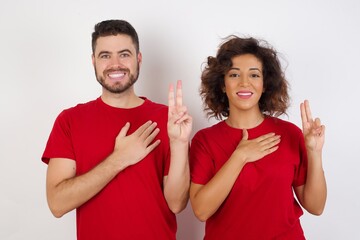 Young beautiful couple wearing red t-shirt on white background smiling swearing with hand on chest...