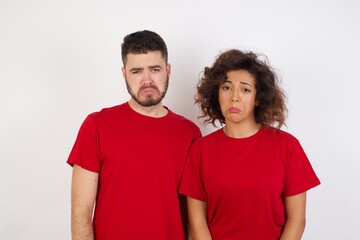Portrait of displeased upset Young beautiful couple wearing red t-shirt on white frowns face as going to cry, being discontent and unhappy as can't achieve goals,  Disappointed young man has troubles