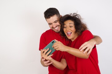 Fototapeta premium Young beautiful couple wearing red t-shirt on white background holding in hands cell playing video games or chatting