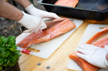 Man hands cutting pink raw salmon with knife on board