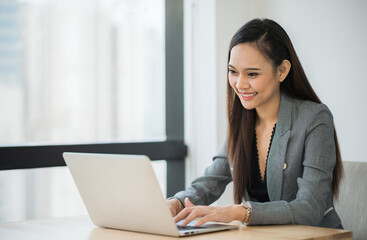 Beautiful asian businesswoman using laptop working in office and smiling.