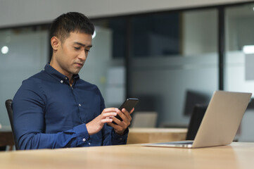 Young asian businessman using smartphone while working in office.