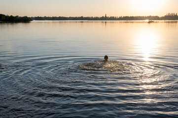 Swimming man in a lake with the setting sun above.