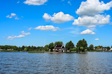 Cute little house on an island in a lake. Blue sky with little white clouds above it. Reeuwijkse plassen, the Netherlands, Europe.