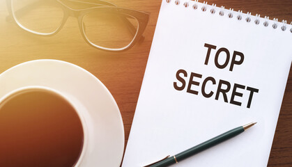 Concept of Top Secret, text Top Secret on notebook with cup of tea and glasses