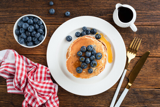 Pancakes with blueberries and maple syrup on a wooden table background, top view