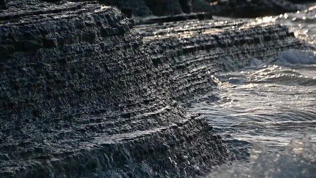 A flysch cliff in Moon Bay, Slovenia that often collapses and is dangerous to humans. Close up view of waves hit sedimentary rock layers. Low angle, slow motion, static shot, shallow depth of field