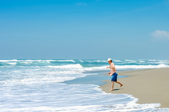 single Chinese young man running and jumping on Parangtritis beach, Yogyakarta, Indonesia.