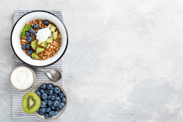 Granola bowl with fruits and yogurt on grey concrete background. Top view, copy space. Healthy eating, sustainable lifestyle concept