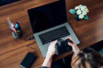 Photographer working on photos on laptop and camera. Woman editing retouching browsing photos working as a freelancer sitting at desk