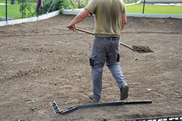 manual worker of a stronger figure throws a soil with a shovel, for a better distribution of the...