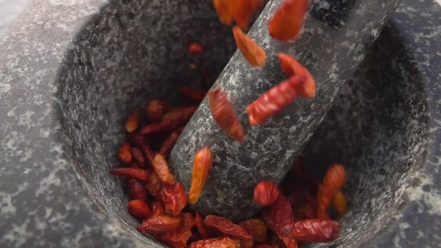 Red cayenne pepper pods are falling into the stone mortar in slow motion