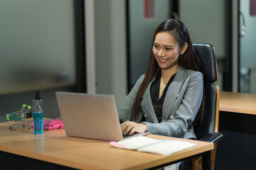 Young asian businesswoman using laptop sitting in modern office working with social distancing alcohol gel on desk.