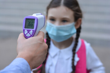 Temperature check in school . Child in medical mask in class in covid-19 outbreak.Teacher with thermometer at preschool or school entrance. Social distancing. Coronavirus prevention.