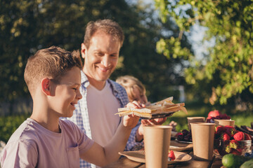 Photo of care loving daddy have summer outdoors picnic lunch share son small kids delicious fresh...