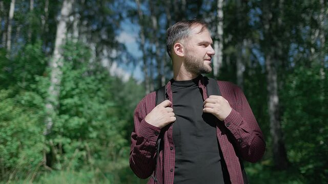 Young handsome bearded man standing in the thicket of the forest looking around with a smile. Summer landscape background. Camping in a forest. High quality 4k footage