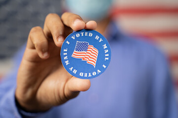 Close up of hands showing I voted by mail sticker with USA flag as background - Concept of US election, mail-in voting or vote by mail