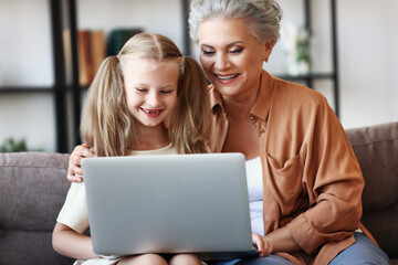 Happy aged woman with granddaughter using laptop at home.