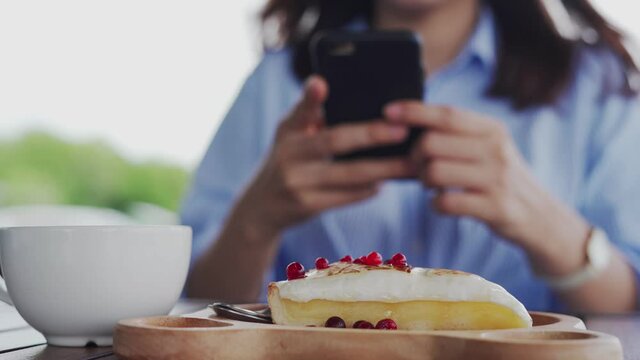 A woman uses a phone to take pictures of strawberry cheesecake. A woman taking pictures of promoting food in a favorite cafe