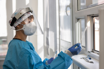 Female doctor holding a nasal swab at a covid-19 testing site window from inside