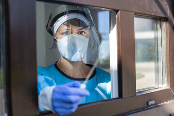 Female doctor holding a nasal swab at a covid-19 testing site window from outside