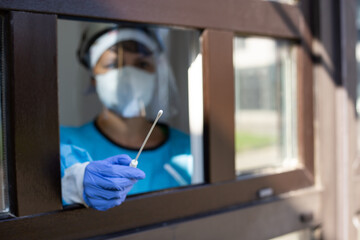 Female doctor holding a nasal swab at a covid-19 testing site window shallow focus 2