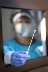 Female doctor holding a nasal swab at a covid-19 testing site window shallow focus