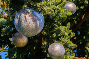 Closeup of many white New Year balls and garland on a branches of artificial Christmas tree outdoors at sunny day.