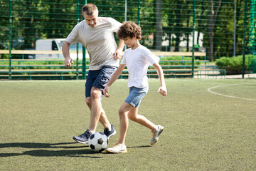 Sportive dad playing soccer with his little son