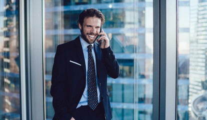 Elegant business man in modern office talking on cellphone laughing cheerfully