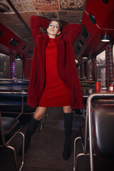Seductive girl in cafe bus (bistro). Retro (vintage) portrait of beautiful stylish young woman in restaurant, wearing red dress, fur coat and boots