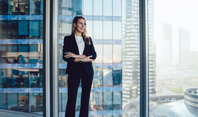 Cheerful businesswoman with crossed arms standing near window in office