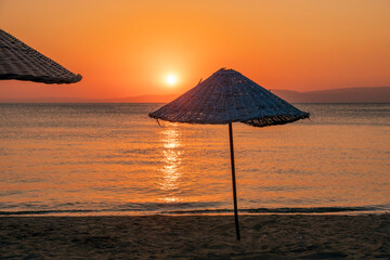 Straw parasol at sand beach with orange sun and sea background at dawn © Stockwars