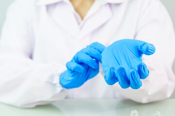 Scientist hands putting in nitrile blue latex gloves in labcoat wearing nitrile gloves
