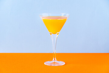 Fresh orange juice in glass on orange surface and light blue background