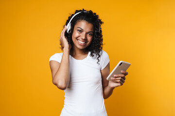 Image of cheerful african american woman using cellphone and headphones