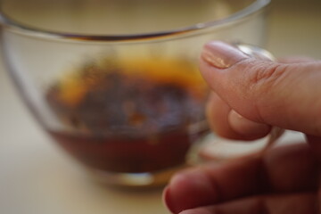 transparent cup with black tea in female fingers on the table.