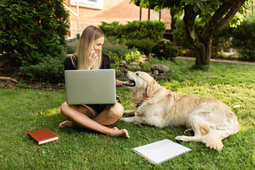 Woman working with laptop and playing with dog Labrador in park