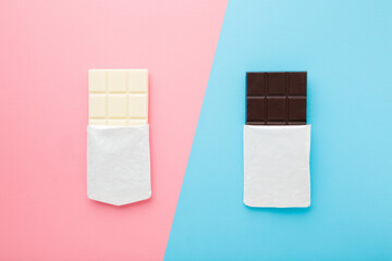 Black and white chocolate bars on light pink blue table background. Pastel color. Opened packs. Sweet snack. Closeup. Top down view.