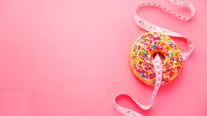 Close up of donuts and measurement tape on pink background.