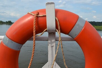 The red or orange lifebuoy hanging on the side of the ship. Red lifebuoy on ship railing with water...